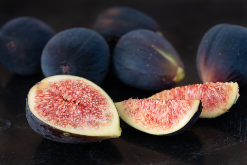 red sliced fresh figs lie next to each other against a dark background. Many figs are also closed behind.