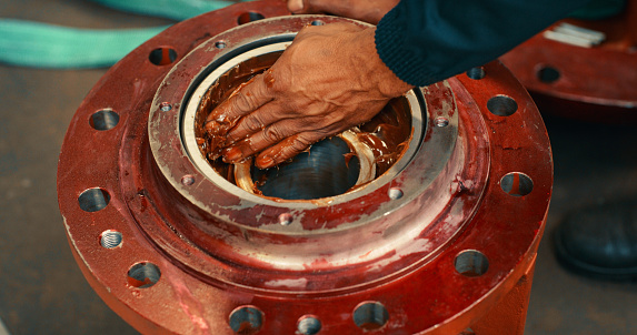 Mechanical engineer hand applying grease, metal oil or lubricant to prevent damage, break or wear and tear of heavy machinery. Closeup of male workshop mechanic fixing factory manufacturing equipment