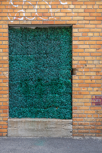 Walled up doorway in a yellow brick wall decorated with green plastic grass