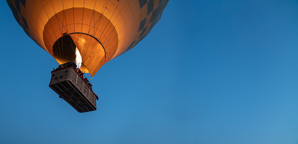 Yellow, red and blue hot air balloon flying overhead in a clear blue sky.