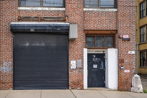 Long Island City, Queens, New York, NY, USA - July 7th 2022: Typical garage entry with a closed gate and a door in an area with small businesses and industries