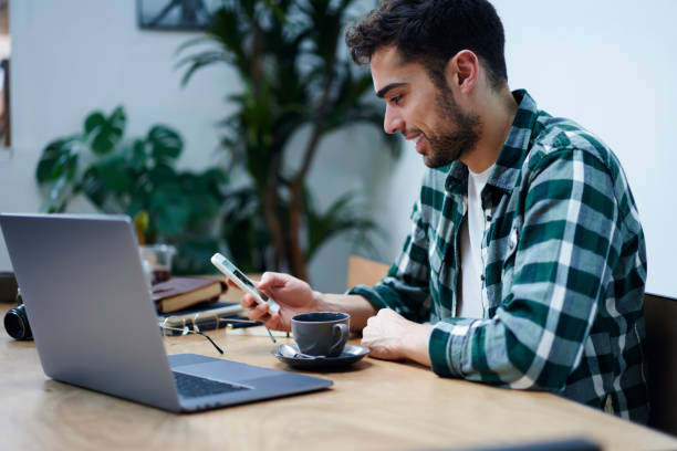 istock Smiling ethnic man with laptop using smartphone 1415372553