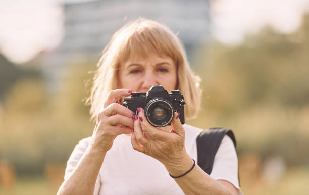 istock Using the camera. Making the photos. Senior woman having nice weekend outdoors on the field at sunny day 1415372556