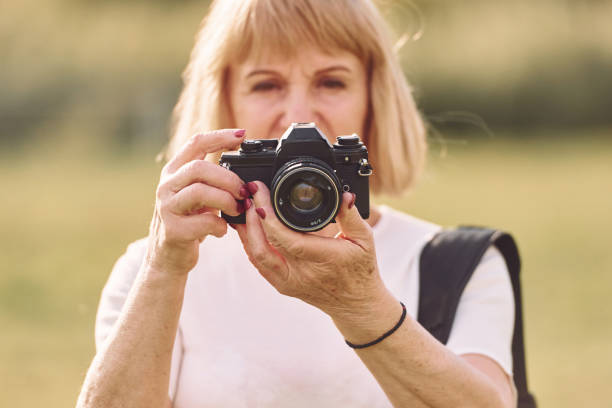 istock Using the camera. Making the photos. Senior woman having nice weekend outdoors on the field at sunny day 1415372577
