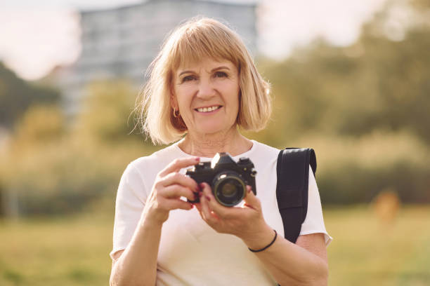 istock Using the camera. Making the photos. Senior woman having nice weekend outdoors on the field at sunny day 1415372578