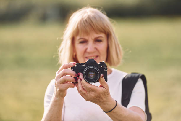 istock Using the camera. Making the photos. Senior woman having nice weekend outdoors on the field at sunny day 1415372583