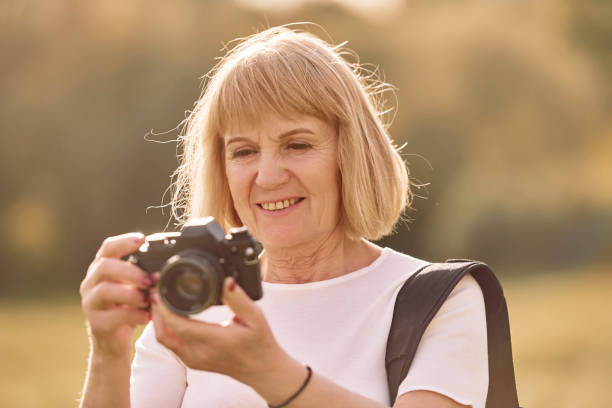 istock Using the camera. Making the photos. Senior woman having nice weekend outdoors on the field at sunny day 1415372600