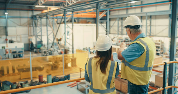 Logistics workers checking stock on tablet, inspecting a factory and organising a warehouse together. Male and female colleagues talking, examining a building and working in a distribution facility stock photo