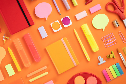 Back to school concept with crayons and school supplies on orange colored background