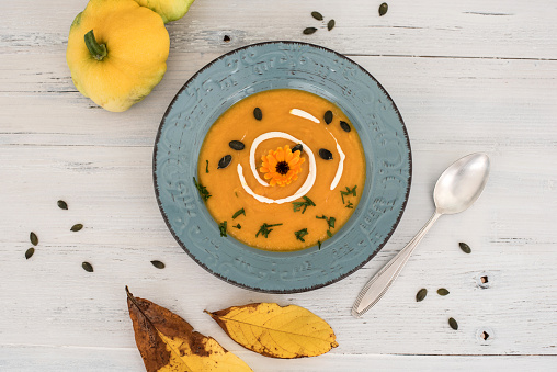 Delicious Pumpkin Soup with Dairy Cream and Pumpkin Seeds on White Wooden Background