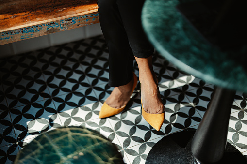 Anonymous photo of a women wearing heels, sitting at the cafe. There is a patterned black and white tile floor.