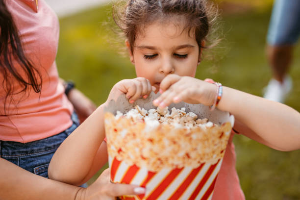 Young daughter eating popcorn with her parents outdoors, on a sunny day. Close-up.
