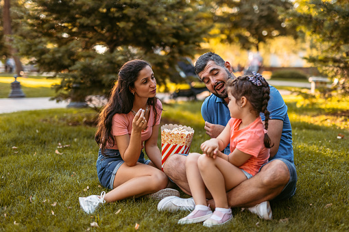 Young father and mother eating popcorn with their daughter outdoors, on a sunny day