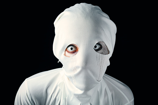 A close up of a creepy person in colored contacts and a ghost costume.