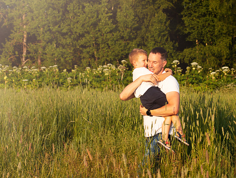 Father and son on the field on the background of the forest. Father holds his son in his arms and hugs. Happy family and parental love concept.