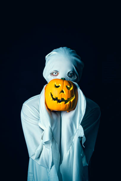 istock Eerie Person Dressed as Ghost Holding Pumpkin 1415378156