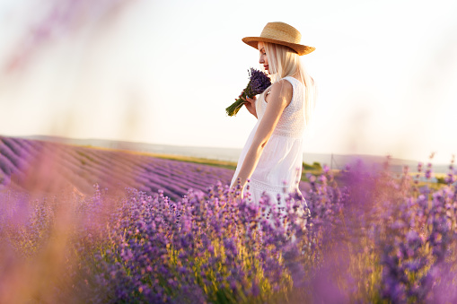 Young woman in long white dress standing in lavender field on sunset