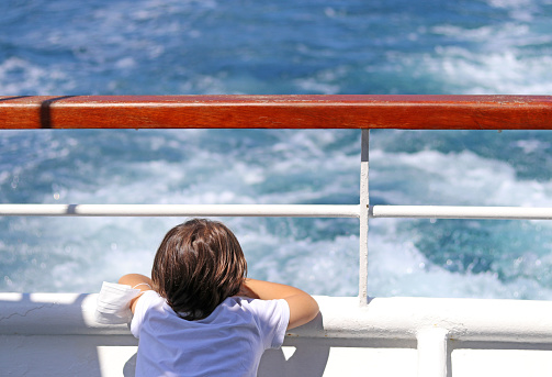 Little boy leaning out of the stern of a ship.