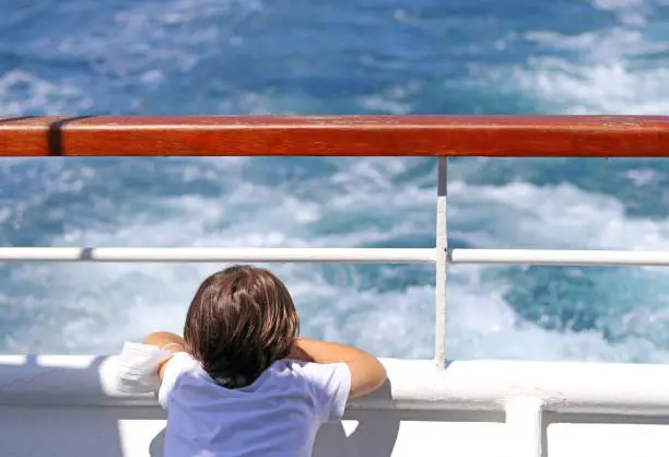 Photo of Little boy leaning out of the stern of a ship.