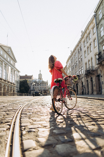 The beautiful woman traveling with the bicycle through the European city at the sunrise