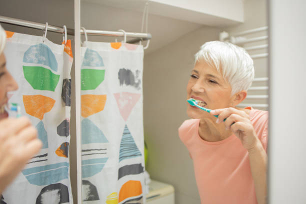 istock Mature woman looking at her reflection while brushing her teeth 1415389452