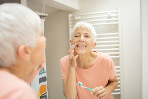 istock Mature woman looking at her reflection while brushing her teeth 1415389512