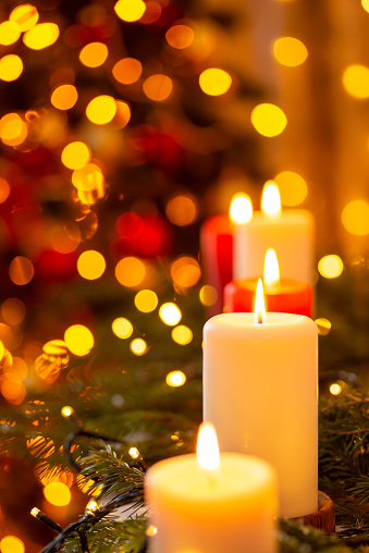 Burning candles surrounded by bright garland lights, vertical shot, copy space