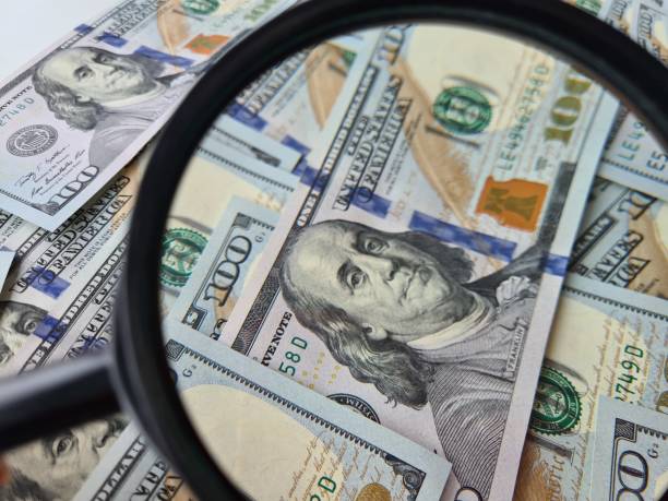 istock Modern currency detector with dollar bills and magnifying glass 1415392865