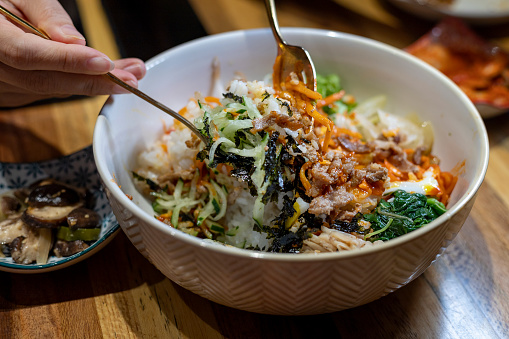 Bibimbap is served as a bowl of warm white rice topped with namul or kimchi and gochujang, soy sauce, or doenjang