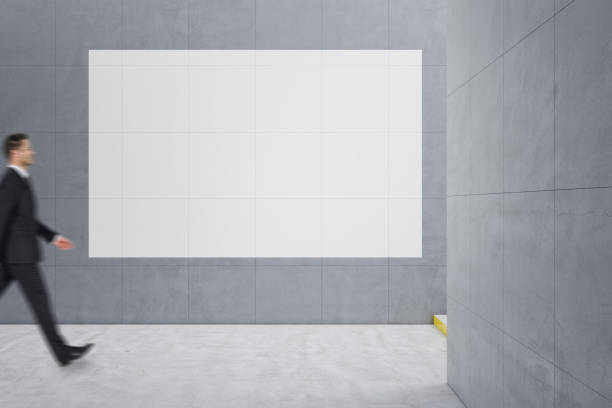 istock Young businessman walking in creative light concrete tile interior with stairs and mock up poster on wall. School hallway and corridor concept. 1415396809
