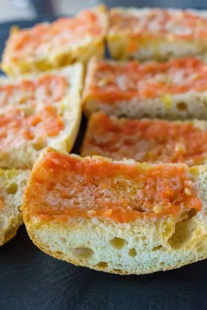 Photo of Pan con tomate, in Catalan, pa amb tomàquet, translated informal pantumaca, traditional in Catalan and Valencian kitchens. It is a slice of bread with ripe tomato rubbed and dressed with olive oil.