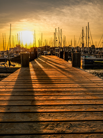 Wooden jetty at Yarmouth harbour on the Isle of wight with boat masts and morning sun rising