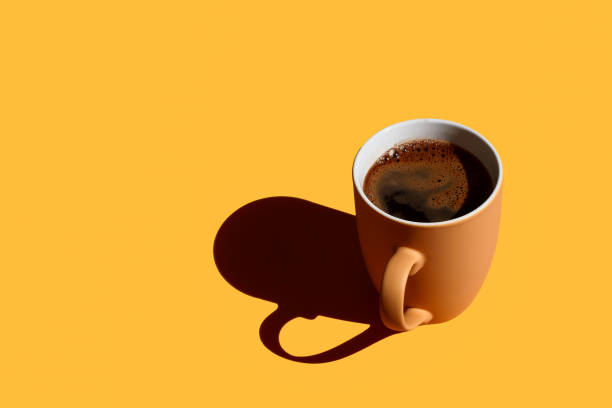 istock Brown mug full of coffee with hard shadow on yellow background with copy space 1415400296