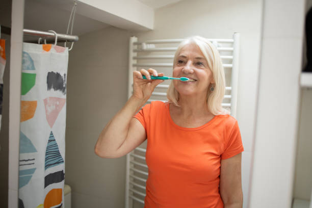 istock Mature woman looking at her reflection while brushing her teeth 1415402505