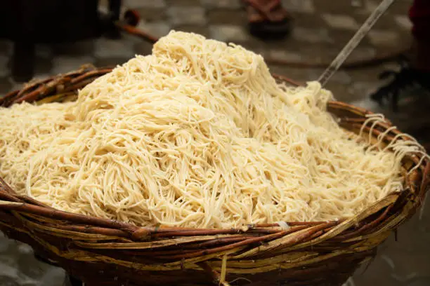 Photo of Chinese Schezwan Also Called Szechwan Veg Hakka Noodles Chowmin or Indian Veg Chow Mein Being Washed Rinsed In Water In Bamboo Basket. Dhaba Style Bulk Preparation For Cooking Street Food In India