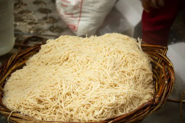 Photo of Chinese Schezwan Also Called Szechwan Veg Hakka Noodles Chowmin or Indian Veg Chow Mein Being Washed Rinsed In Water In Bamboo Basket. Dhaba Style Bulk Preparation For Cooking Street Food In India