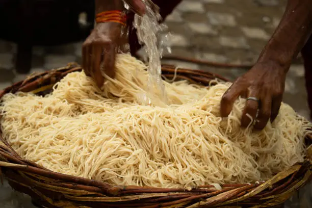 Photo of Chinese Schezwan Also Called Szechwan Veg Hakka Noodles Chowmin or Indian Veg Chow Mein Being Washed Rinsed In Water In Bamboo Basket. Dhaba Style Bulk Preparation For Cooking Street Food In India