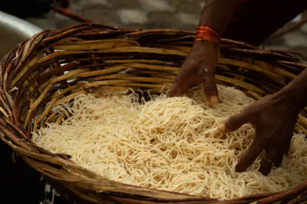 Photo of Chinese Schezwan Also Called Szechwan Veg Hakka Noodles Chowmin or Indian Veg Chow Mein Being Washed Rinsed In Water In Bamboo Basket. Dhaba Style Bulk Preparation For Cooking Street Food In India