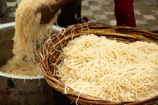 Photo of Chinese Schezwan Also Called Szechwan Veg Hakka Noodles Chowmin or Indian Veg Chow Mein Being Washed Rinsed In Water In Bamboo Basket. Dhaba Style Bulk Preparation For Cooking Street Food In India