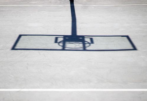 No people, just shadow of a hoop and rim in a basketball court