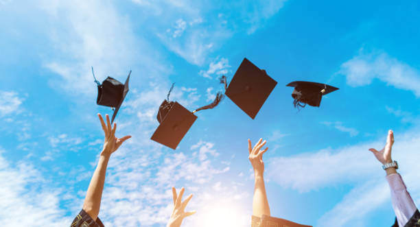 istock Four graduates throwing graduation hats in the air 1415405888
