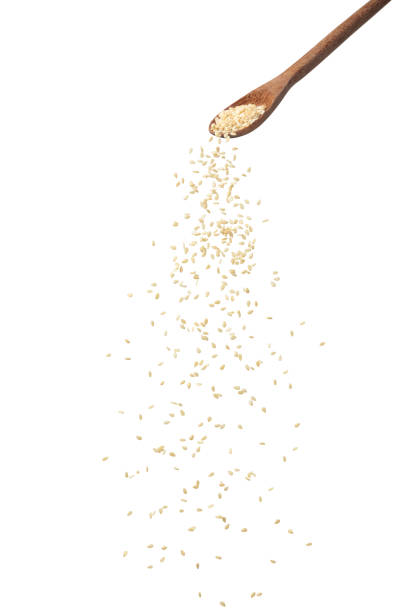 white sesame seeds pour from a wooden spoon