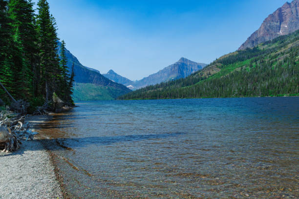 Lake with high mountains in Glacier National Park, Montana. Blue sky with clouds and foliage trees
