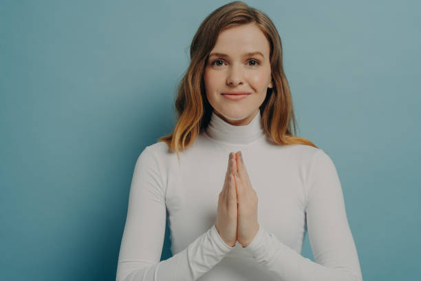istock Young pleaded trustful woman posing with hands folded in praying gesture, isolated on blue 1415408877