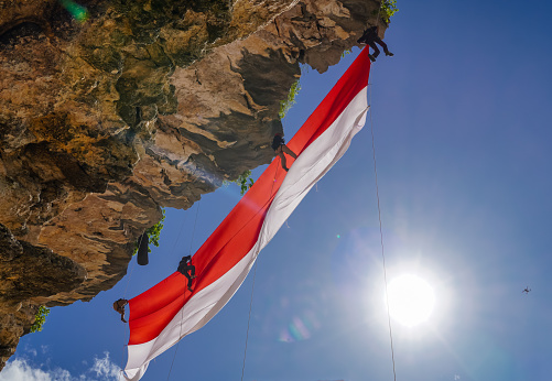 Aceh Besar, Indonesia - August 17, 2022  : In commemoration of the Independence Day of the Republic of Indonesia, Nature Lovers Student Movement (Gainpala) UIN Ar-Raniry Banda Aceh raised a giant red and white Indonesian flag, at Tebing Lampuuk Beach