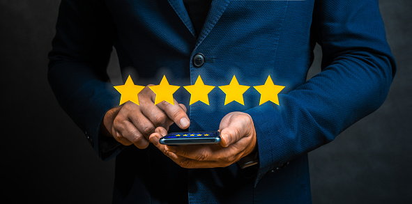 Businessman pointing five star symbol to increase rating of company. Man Evaluating Mobile Application On Smartphone With Five Stars. Customer review rating on phone business concept