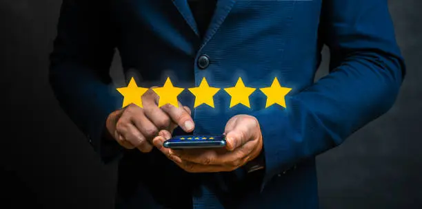 Photo of Businessman customer giving five star rating on cellphone. Review, Service rating, satisfaction, Customer service experience and satisfaction survey concept. dark blue tone