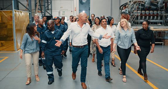 Happy, excited and smiling workers walking around modern industrial warehouse. Group, team or coworkers on factory floor taking a tour. Professional manager leading employees around work building.