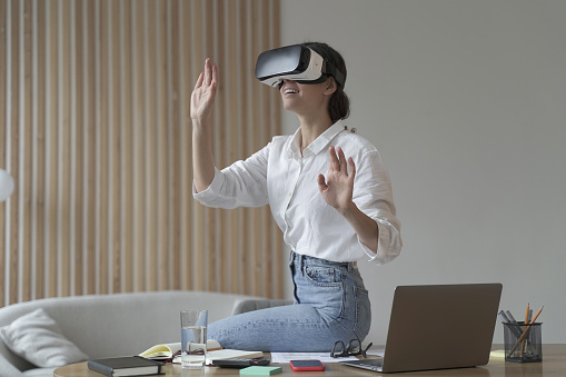 Employee experience with virtual reality. Impressed business woman sitting on office table, using vr glasses goggles at work, testing innovative method for business, interacting with digital interface