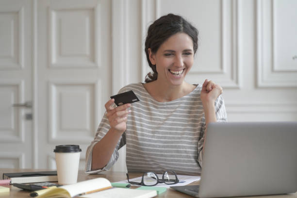 młoda szczęśliwa hiszpanka trzyma kartę kredytową i czuje się podekscytowana podczas robienia zakupów online na laptopie - hiszpanka_& zdjęcia i obrazy z banku zdjęć
